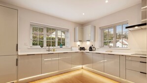 Une cuisine moderne avec des meubles blancs, un plancher en bois et deux fenêtres équipées de stores.