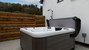 Un bain à remous avec une terrasse en bois et un mur blanc en arrière-plan.