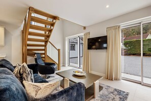 Una sala de estar moderna con una escalera de madera, un sofá, una mesa y un televisor instalado en la pared.