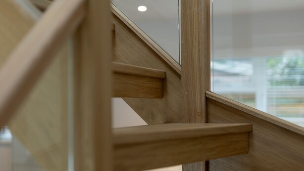 Un escalier en bois avec des rampes en verre, menant à l’étage supérieur.