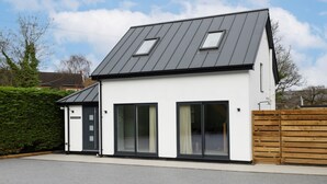 Une maison moderne à deux étages, dotée d’un toit en pente, de grandes fenêtres et d’une clôture en bois.
