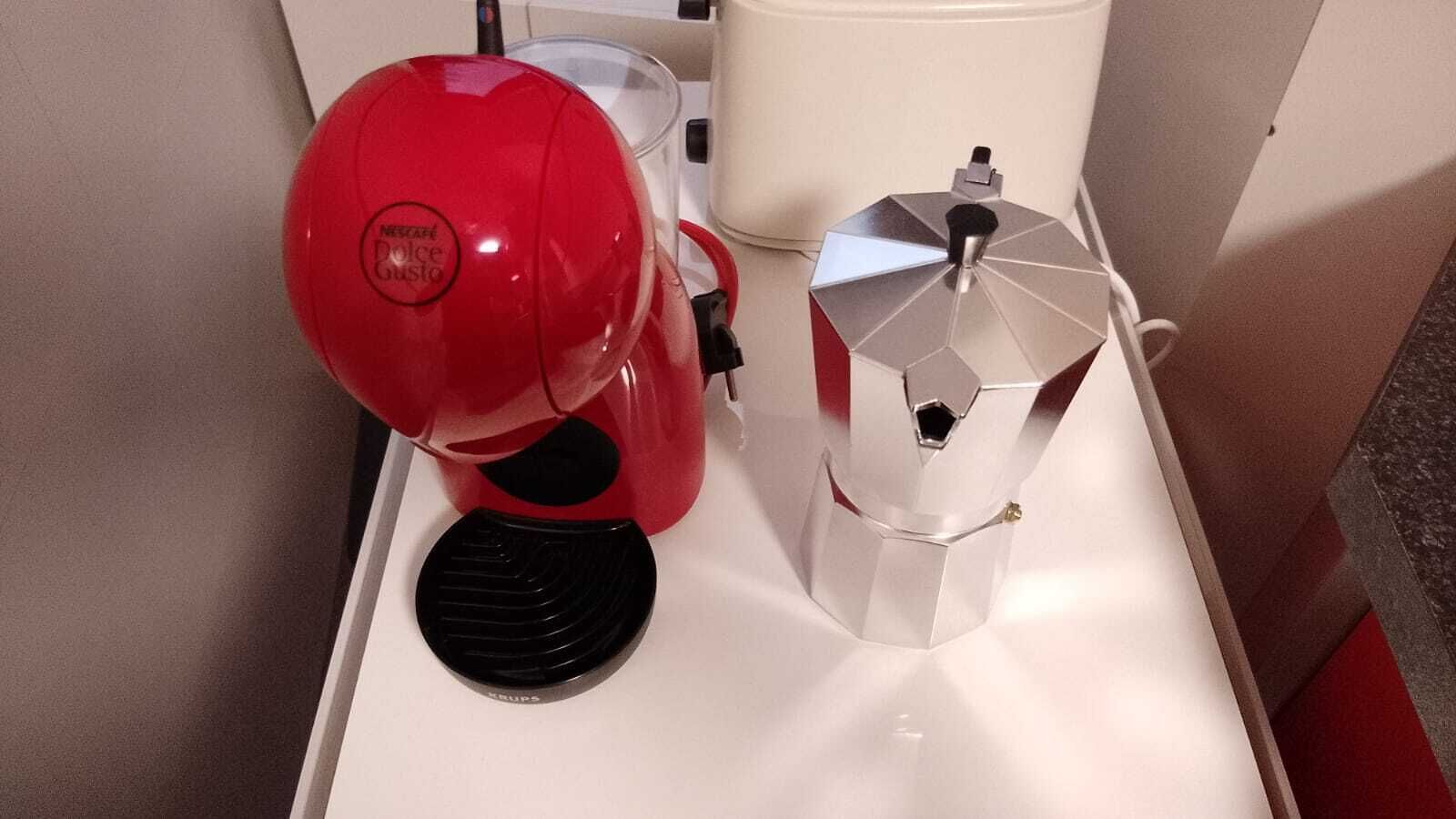 Una máquina de espresso roja y una cafetera plateada sobre una encimera blanca.
