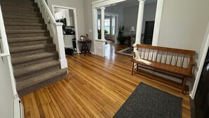 A spacious living area with a wooden floor, a bench, and a staircase leading to a kitchen. - Cozy Home in Holyoke with 3 bedrooms (Holyoke)