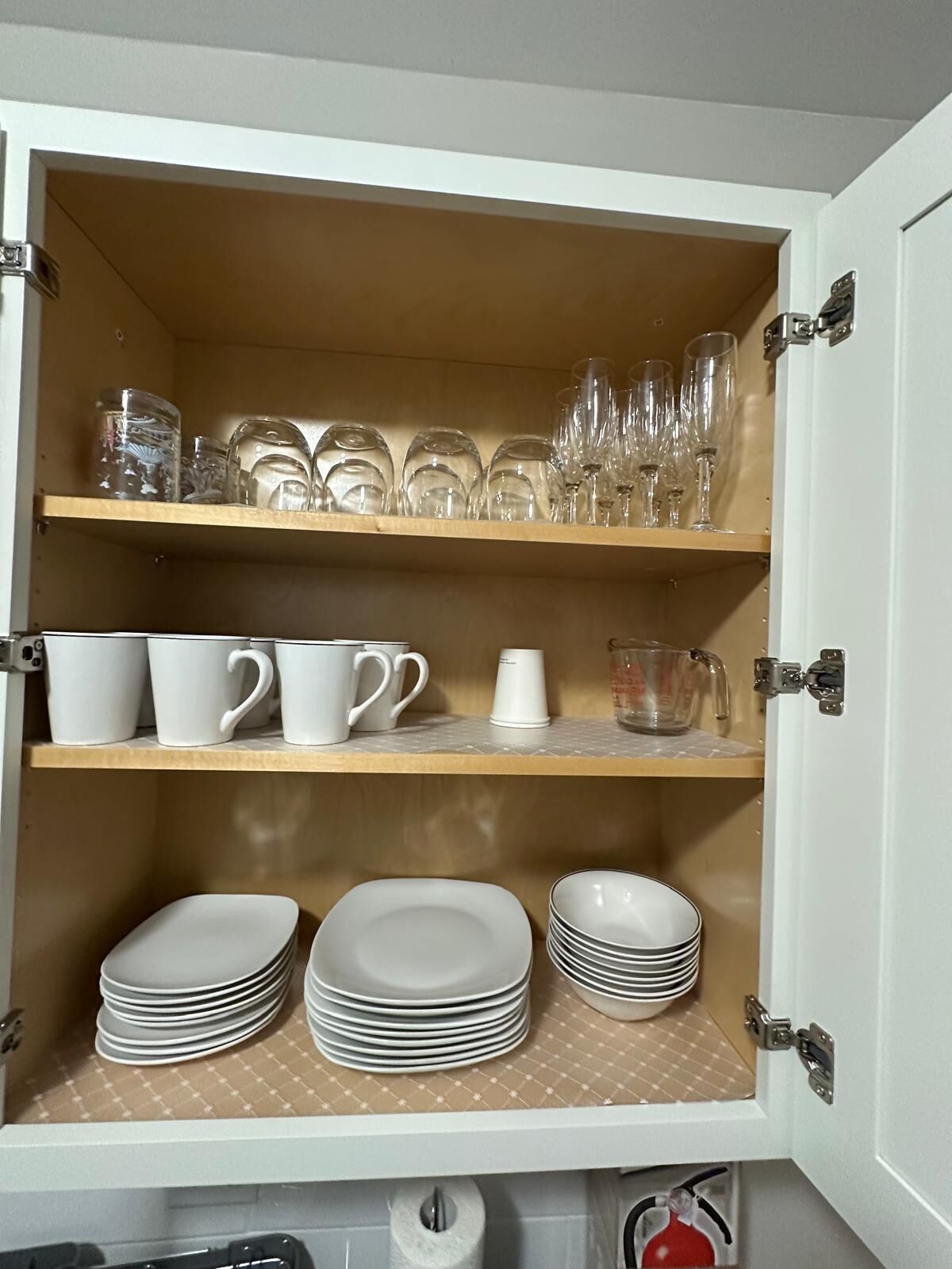 Un meuble avec des étagères où sont rangées des tasses, des verres et des assiettes blancs.