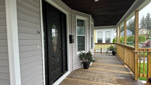 A covered porch with a wooden floor, a black door, and a number '36' on the wall. - Cozy Home in Holyoke with 3 bedrooms (Holyoke)