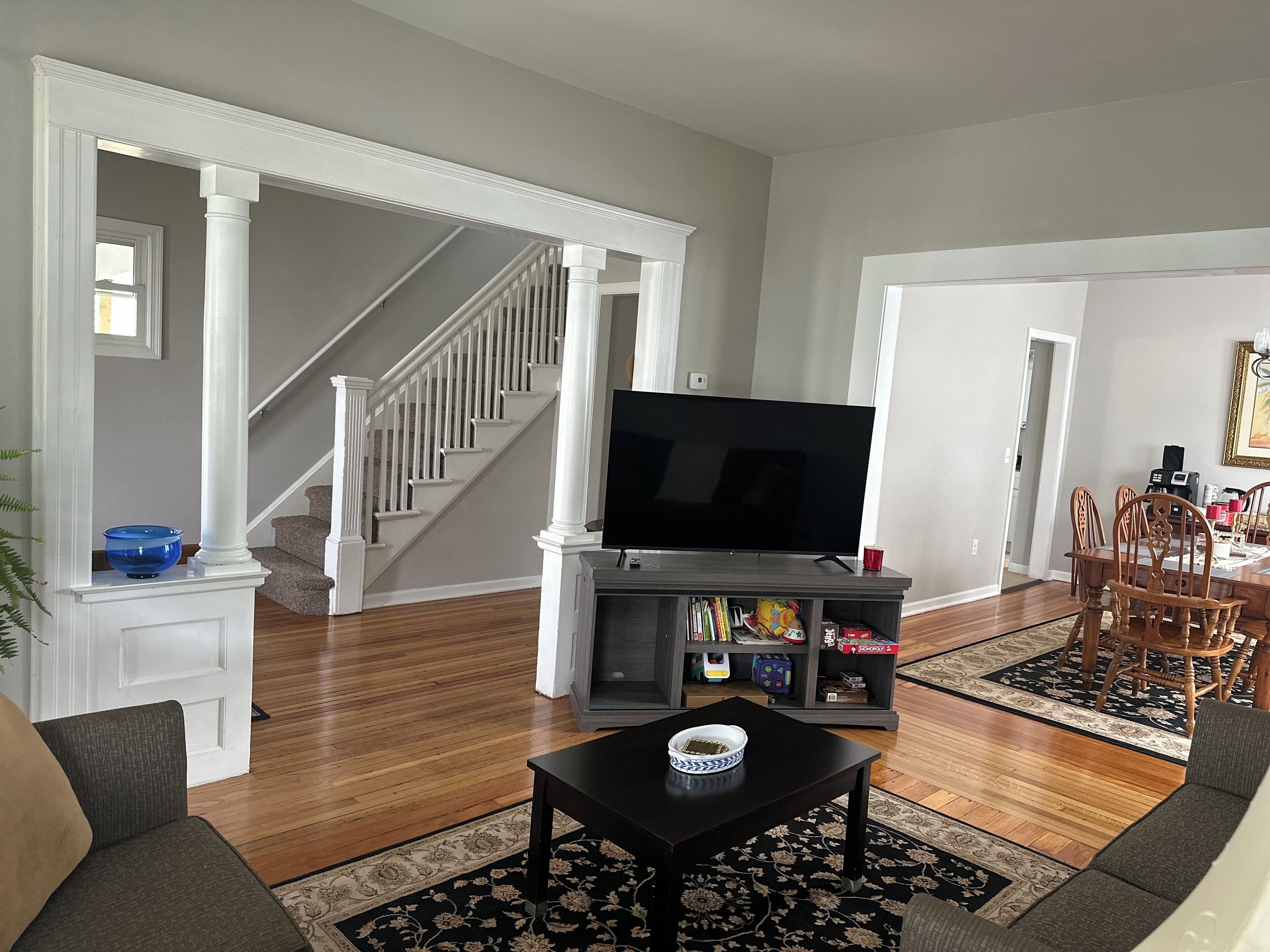 Una sala de estar con una escalera, un televisor de pantalla plana, una mesa de centro y un comedor con sillas y una mesa.