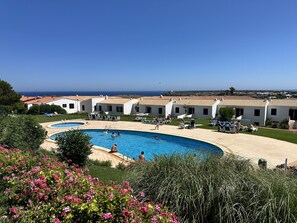 A resort with a large swimming pool, multiple lounge areas, and a view of the sea.