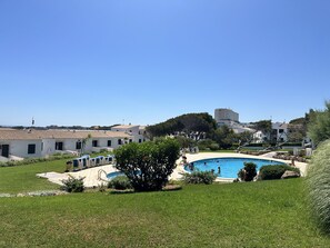 A swimming pool surrounded by a grassy area, with buildings in the background.