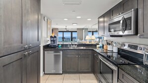 Una cocina moderna con armarios oscuros, electrodomésticos de acero inoxidable y un amplio ventanal con vistas al océano.