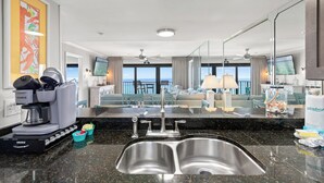 Habitación de hotel con kitchenette, un espejo grande, un lavamanos, ventilador de techo y vista al océano.