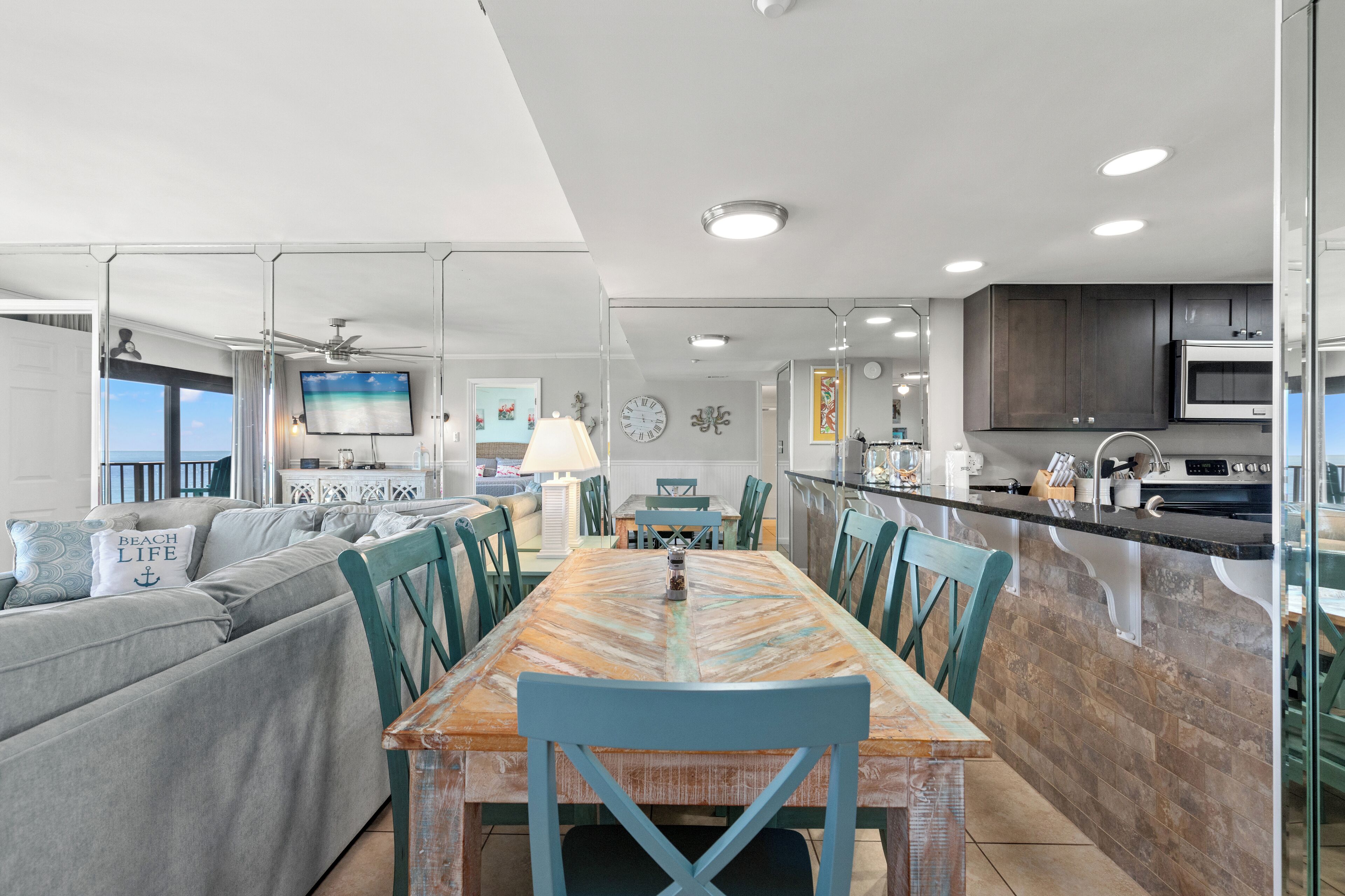 A modern kitchen with a dining area, featuring a large island, dark cabinets, and a flat-screen TV.