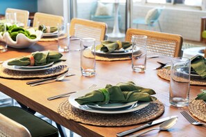 Una mesa de comedor dispuesta con platos, cubiertos y vasos, con individuales tejidos y servilletas verdes.