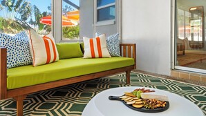 Un sofá verde con almohadas a rayas, una mesa blanca con una tabla de quesos y una alfombra estampada.