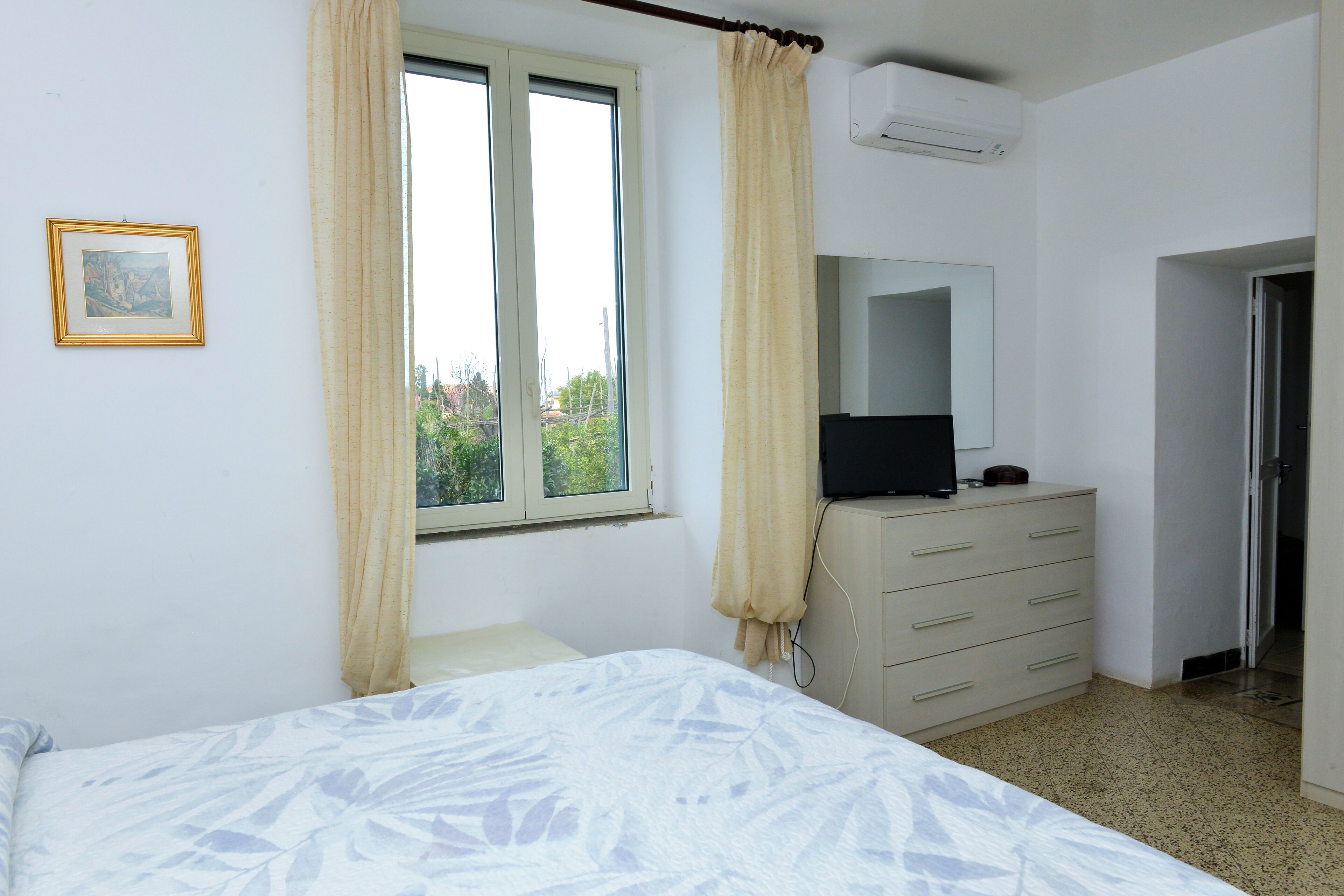 A bedroom with a bed, a dresser, a TV, and a window with curtains.