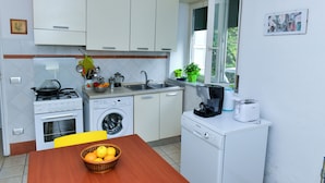 A compact kitchen with white cabinets, a stove, a washing machine, and a coffee maker. - I Giardini di Daphne (Meta)