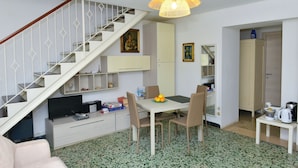 A modern living room with a staircase, a dining area with a table and chairs, and a kitchen area with a coffee maker and kettle. - I Giardini di Daphne (Meta)