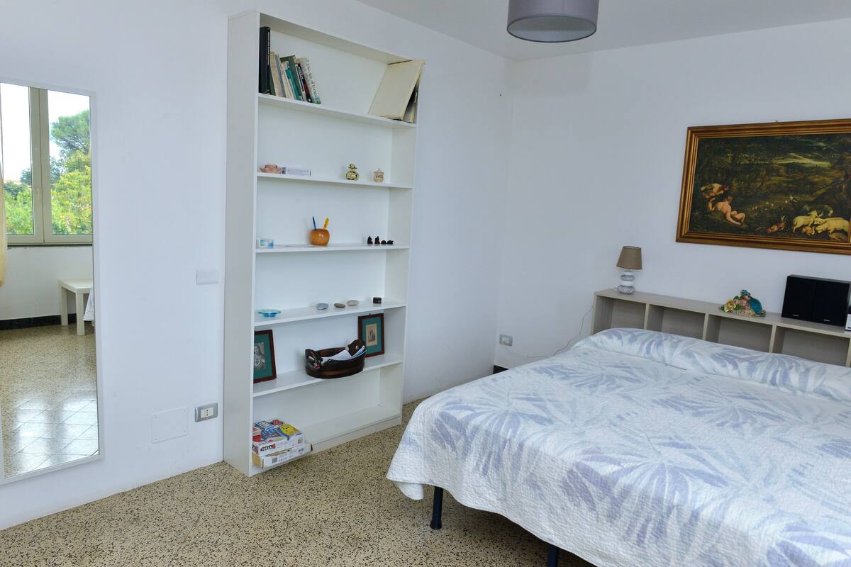 A bedroom with a bed, a bookshelf, a desk, and a painting on the wall.