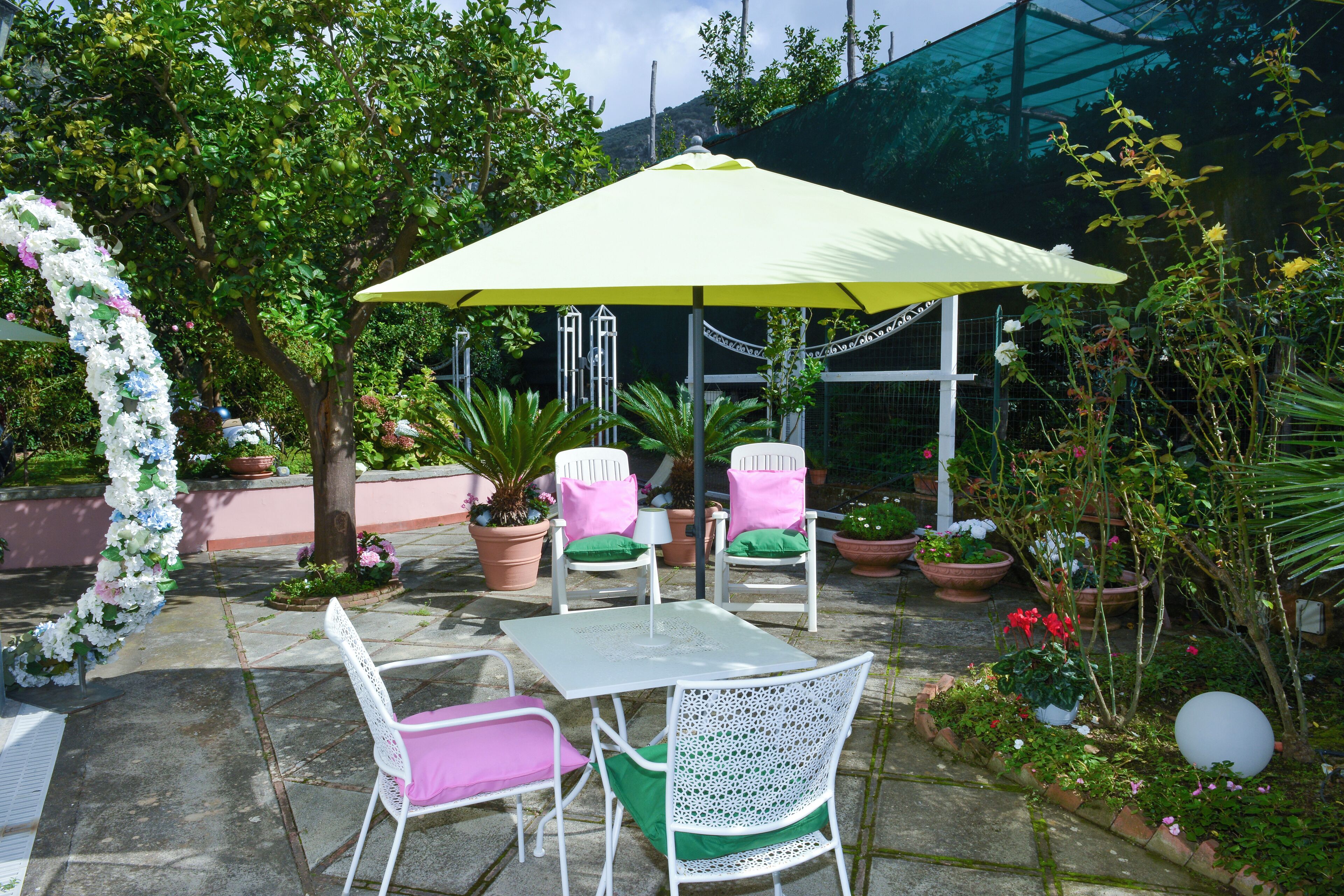 Une terrasse extérieure avec une table et des chaises, entourée de plantes en pot et agrémentée d’une arche décorative.