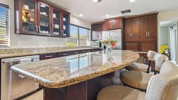 Una cocina con alacenas de madera oscura, encimera de granito y una isla central con asientos.
