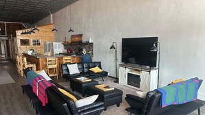 Een moderne woonkamer met zwarte leren banken, een flatscreen televisie en een keuken met houten keukenkastjes en een bar.