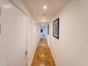 Een gang met houten vloer, witte wanden en kunstwerken in lijsten.