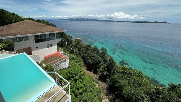 A coastal property with a swimming pool, a balcony, and a view of the sea and distant islands.