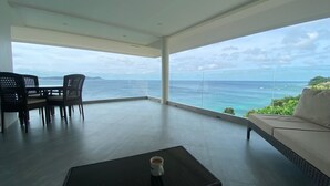 A spacious balcony with a view of the ocean, a dining area with chairs, and a sofa.