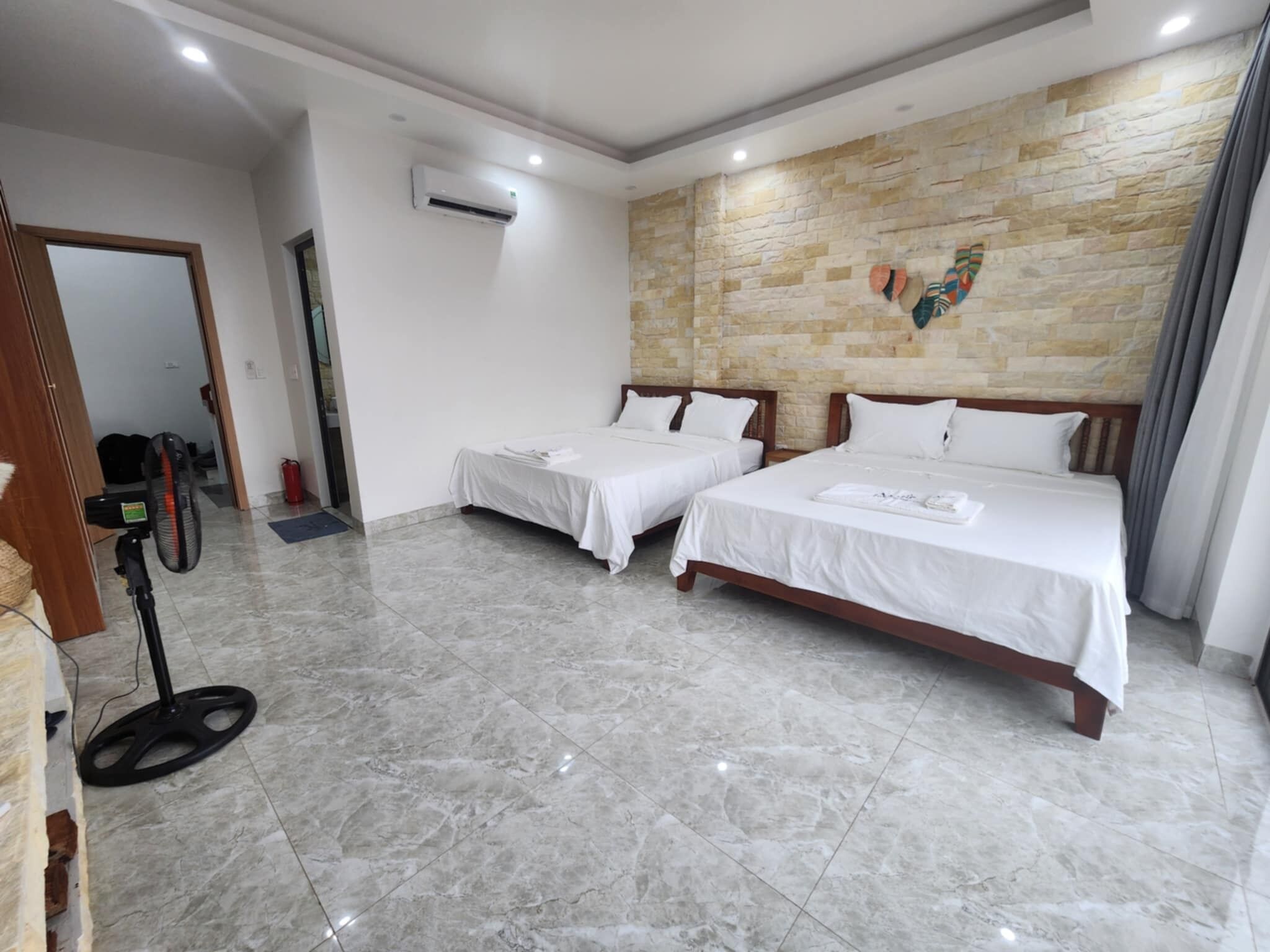 A hotel room with two beds, a stone wall, and a ceiling fan.