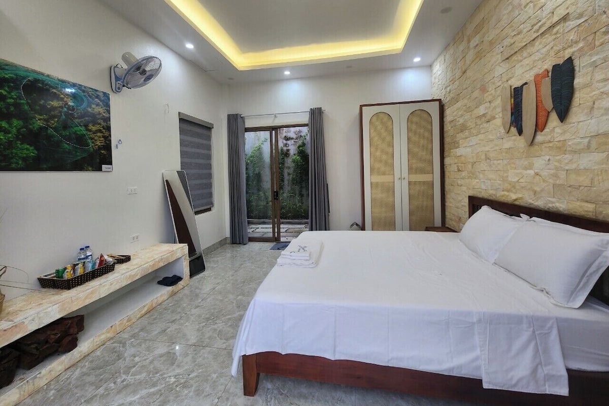 Un dormitorio con cama, una banca con artículos de aseo, un ventilador y vistas al exterior.