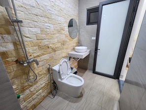 A bathroom with a stone wall, a toilet, a sink, and a shower. - Vu's Homestay Tam Coc (Nam Hoa Lu)