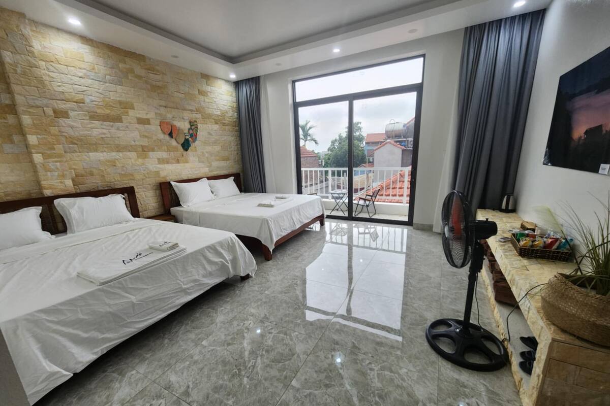 Habitación de hotel con dos camas, balcón, ventilador y vistas al exterior.