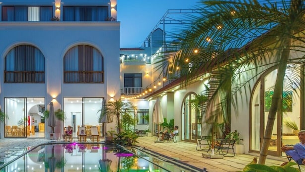 A swimming pool with a curved edge, surrounded by palm trees and outdoor seating. - Vu's Homestay Tam Coc (Nam Hoa Lu)