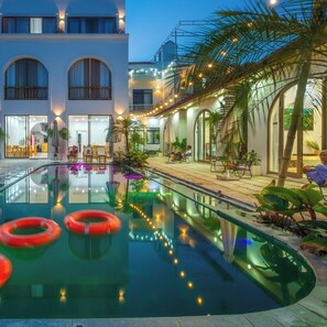 Una piscina con borde curvo, rodeada de palmeras y mobiliario exterior.