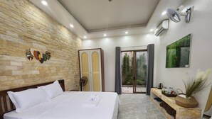 A modern bedroom with a large bed, stone wall, and a sliding glass door leading to a balcony. - Vu's Homestay Tam Coc (Nam Hoa Lu)