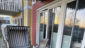 A wooden deck with a table and two chairs, a striped cushioned bench, and a sliding glass door.