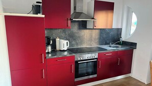 A compact kitchen with red cabinets, a stainless steel oven, and a black countertop.