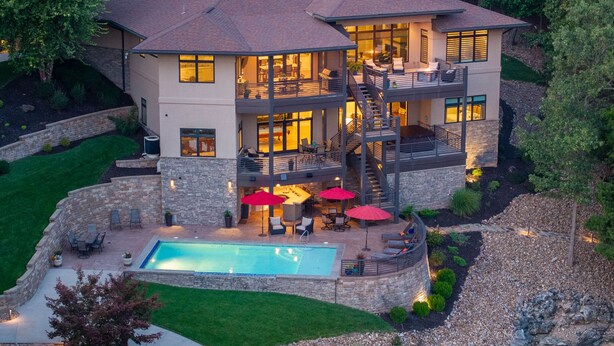 A multi-story house with a swimming pool, outdoor seating, and a stone retaining wall. - Luxury Lakefront Home with Heated Pool and Protected Cove (Sunrise Beach)