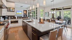 A modern kitchen with a large island, stainless steel appliances, and a dining area with wooden tables and chairs. - Luxury Lakefront Home with Heated Pool and Protected Cove (Sunrise Beach)