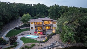 A two-story house with a swimming pool, surrounded by a landscaped garden and a body of water. - Luxury Lakefront Home with Heated Pool and Protected Cove (Sunrise Beach)