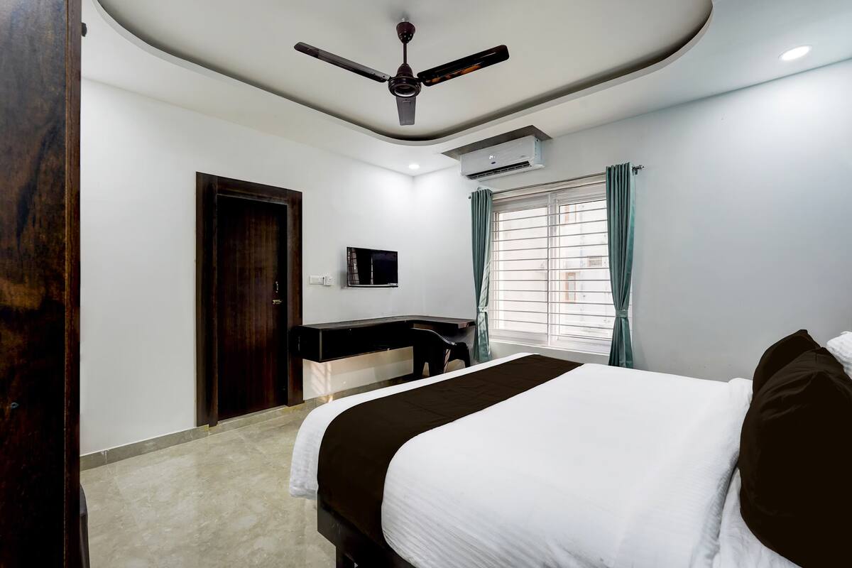 Une chambre à coucher comprenant un lit, un bureau, un ventilateur de plafond, un climatiseur et une fenêtre avec des rideaux.