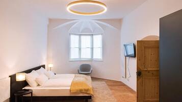 Quarto com cama, luminárias de cabeceira, uma cadeira, televisão e porta de madeira.