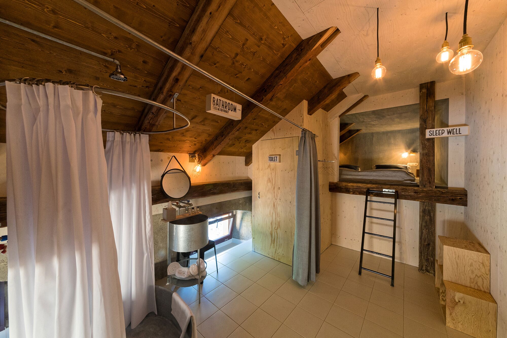 Een eenvoudige badkamer met een douche, toilet en een stapelbed waarop 'slaap zacht' staat.
