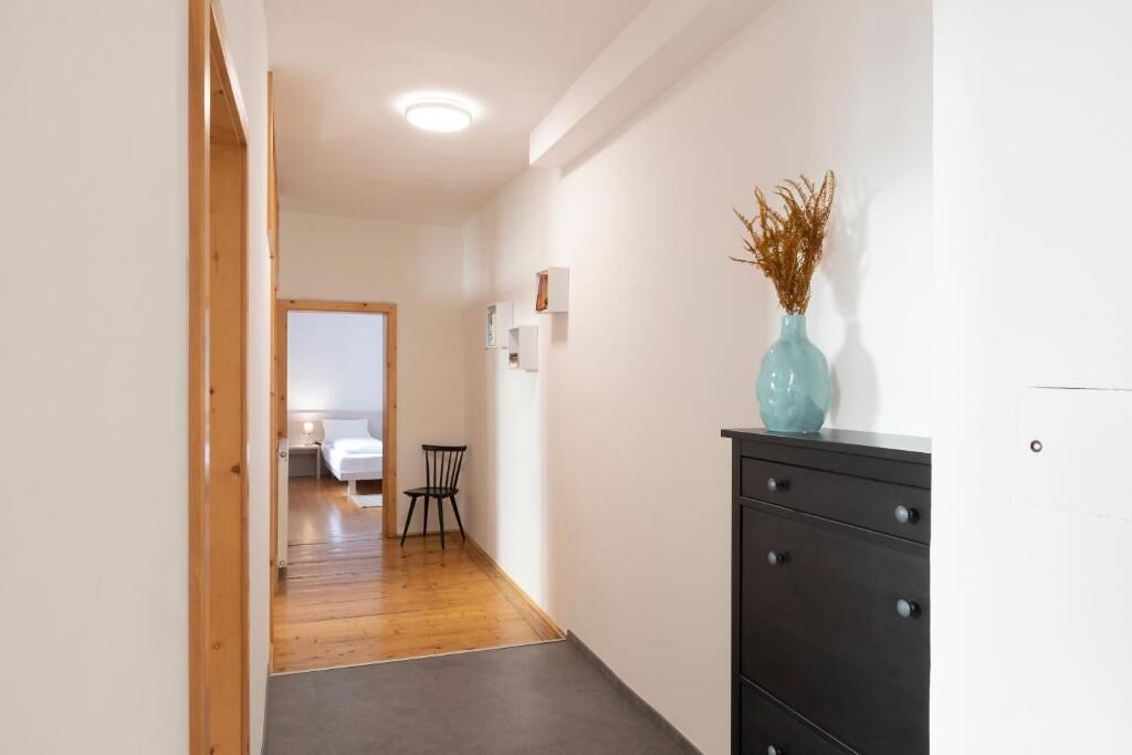 Ein Flur mit Holzboden, einem schwarzen Schminktisch mit einer Vase und einem Bett im Hintergrund.
