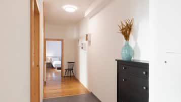 Ein Flur mit Holzboden, einem schwarzen Schminktisch mit einer Vase und einem Bett im Hintergrund.