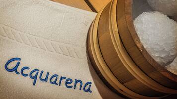 A towel with "Acquarena" embroidered in blue, a wooden bowl with ice cubes, and a wooden surface.