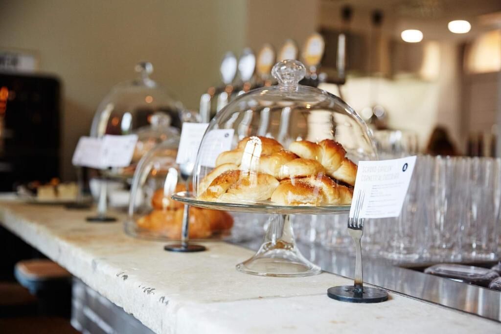 Un comptoir de buffet où sont présentés divers pâtisseries sous des cloches de verre, avec les prix clairement indiqués.