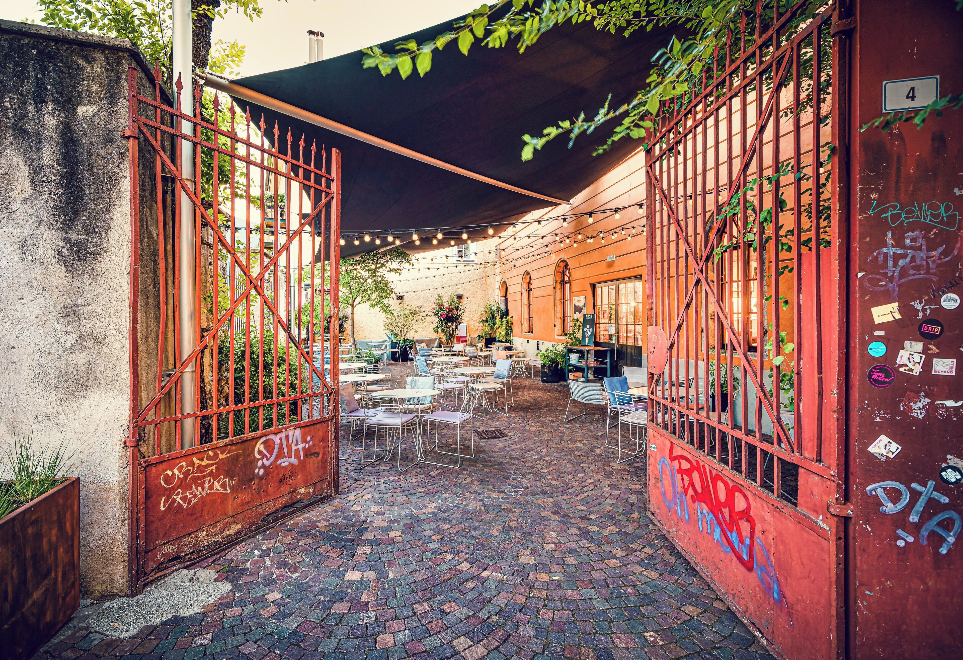 An outdoor café with brick flooring, metal tables and chairs, and a covered area with string lights.