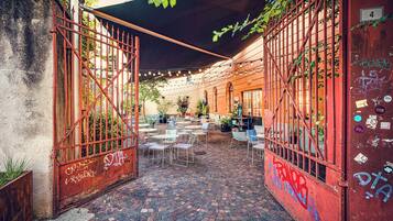 An outdoor café with brick flooring, metal tables and chairs, and a covered area with string lights.