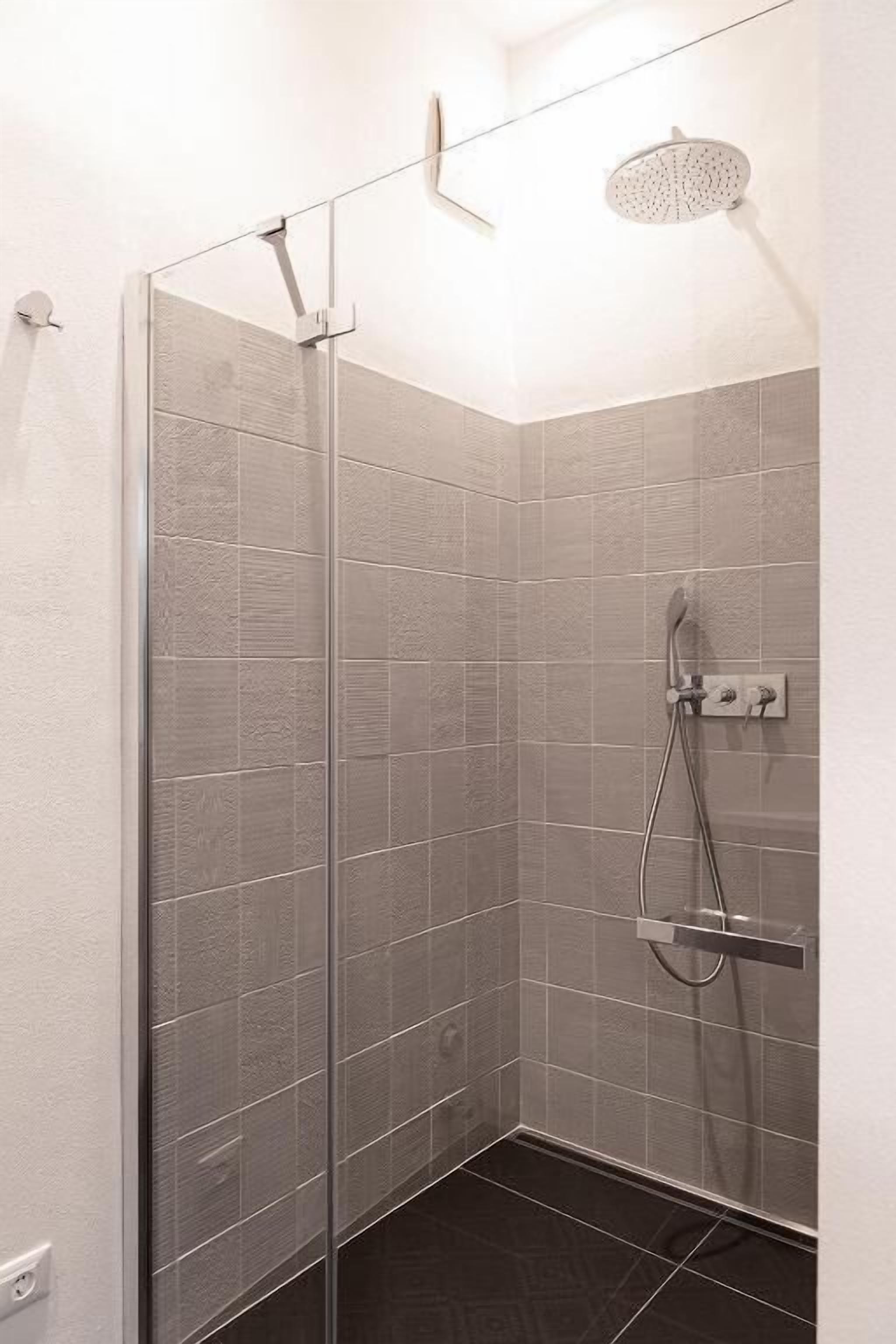 A glass-enclosed shower with a handheld showerhead and a wall-mounted control panel.