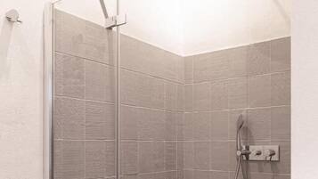 A glass-enclosed shower with a handheld showerhead and a wall-mounted control panel.